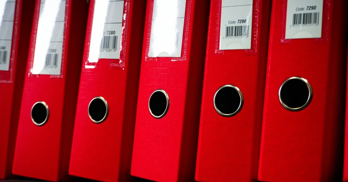 Red binders on a shelf. The AI Act does not ask for a thick archive, it asks for a few fixed documents in a fixed place.