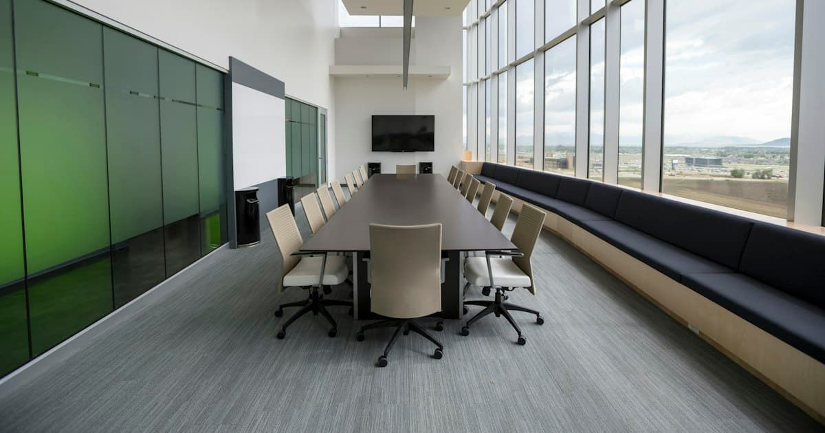 An empty boardroom with a long table. The decision is made in the conversations before anyone sits down here.